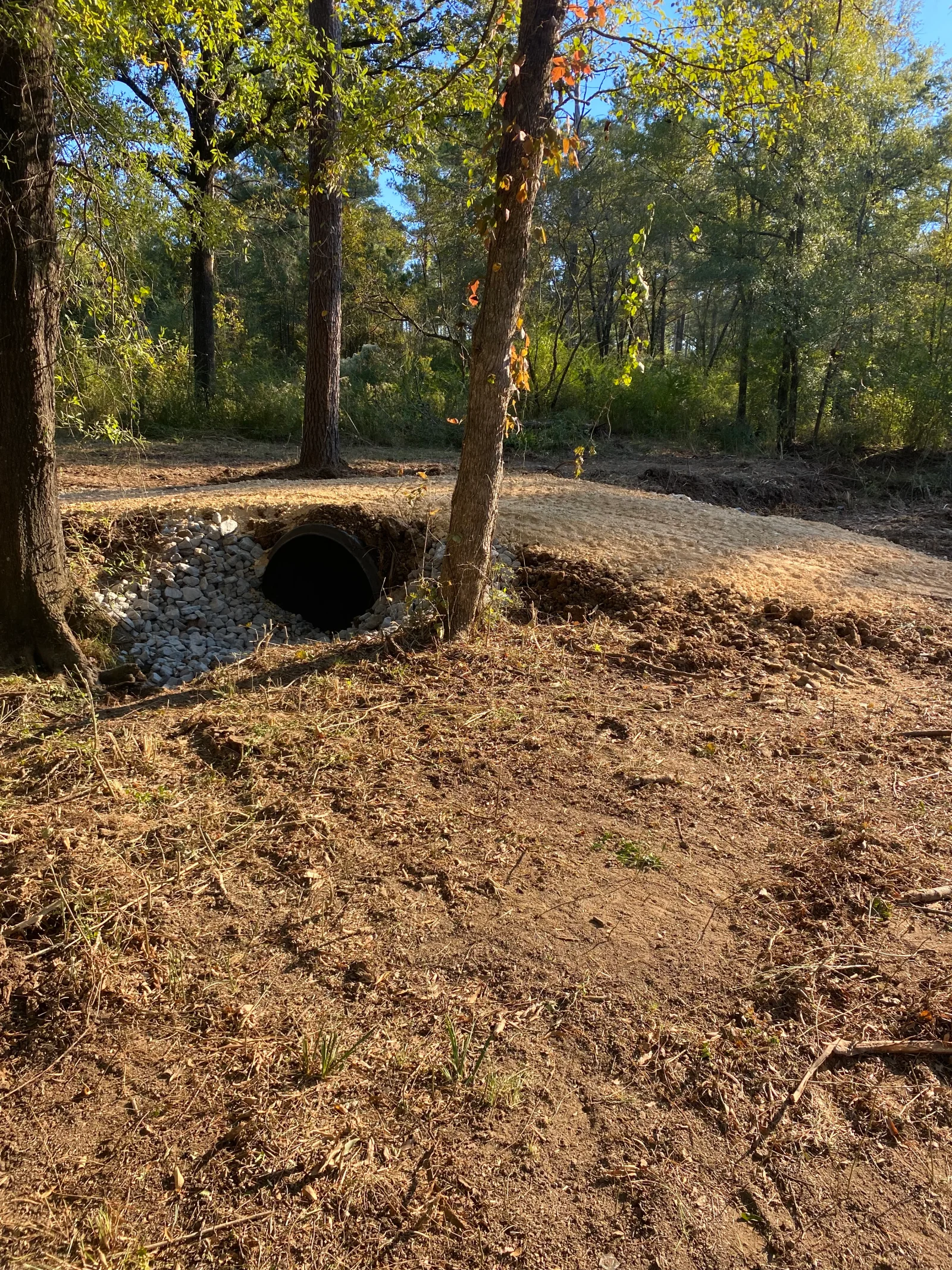 Corrugated metal culvert installed in wooded area with gravel base and excavated drainage channel