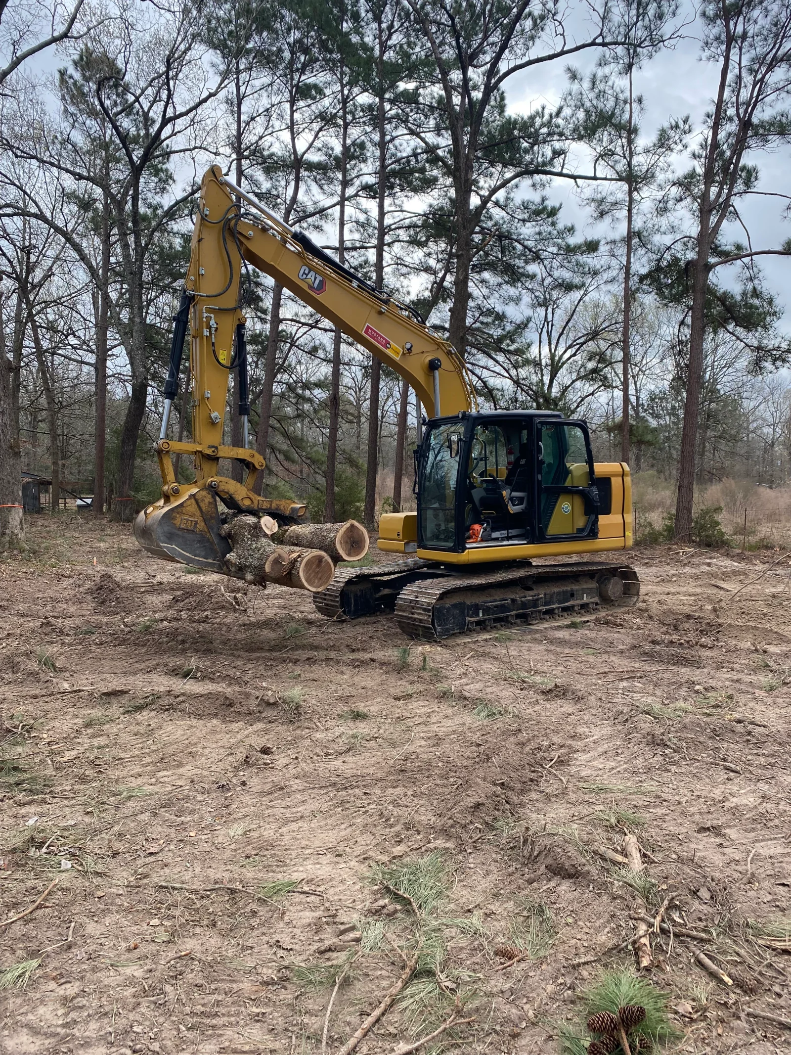 CAT excavator with grapple bucket holding felled logs during land clearing operation