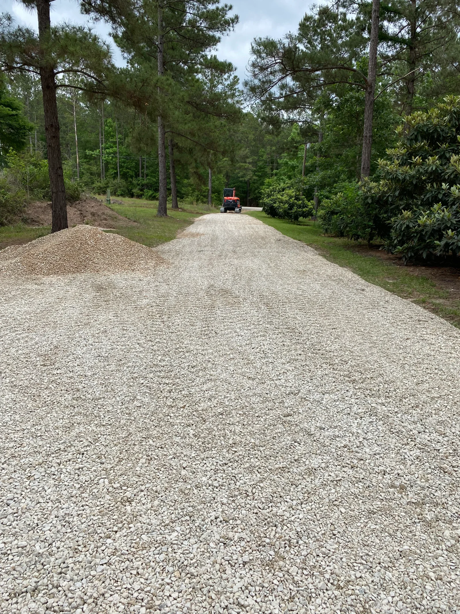 Freshly graded gravel driveway with crushed stone base through forested property with tall pines