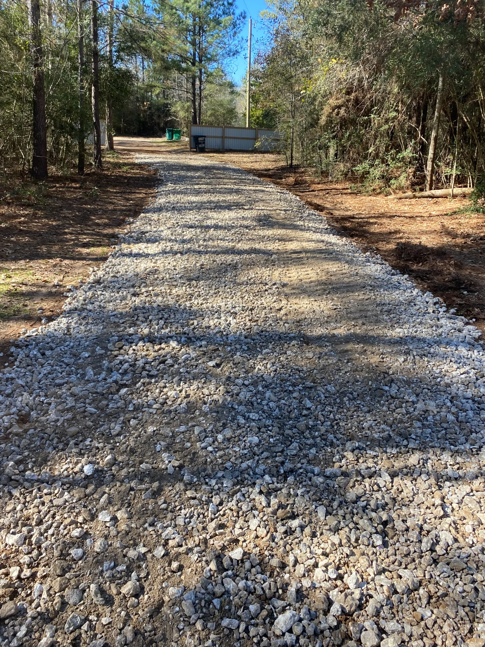 Compacted gravel driveway through wooded area with cleared shoulders and drainage base