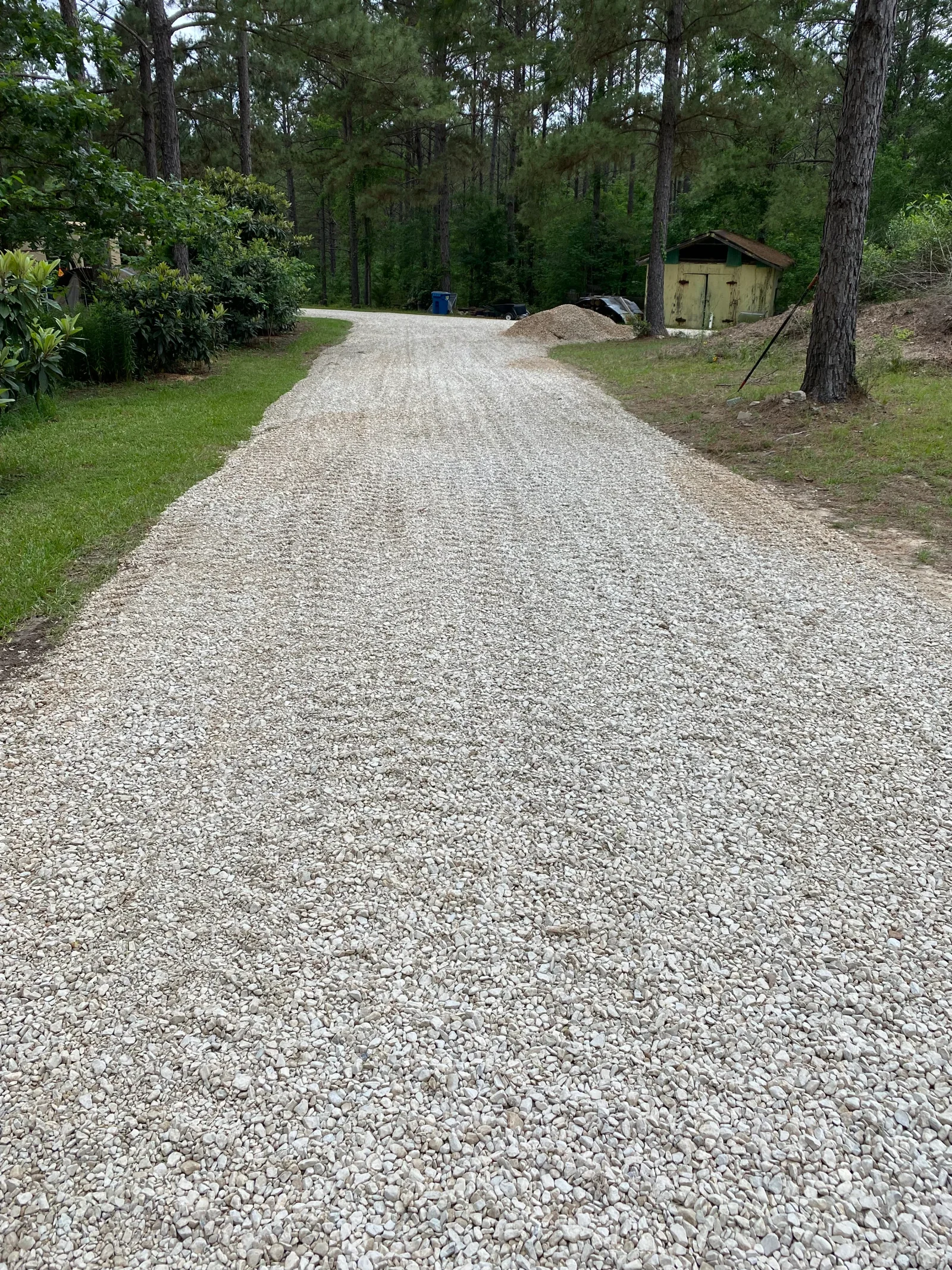 Compacted crushed stone driveway winding through wooded lot with mature trees