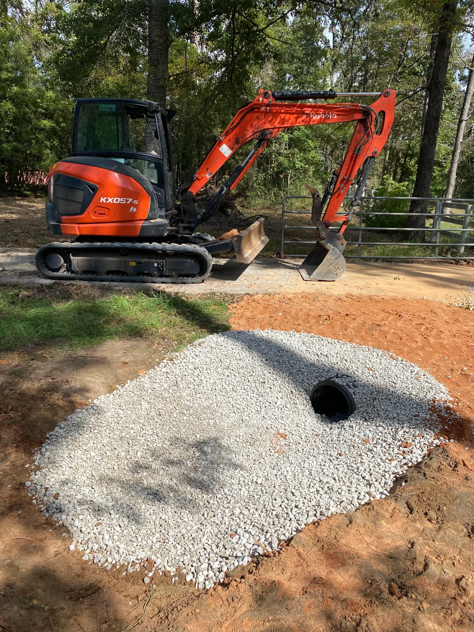 Compact excavator positioning white drainage rock around perforated septic pipe during installation