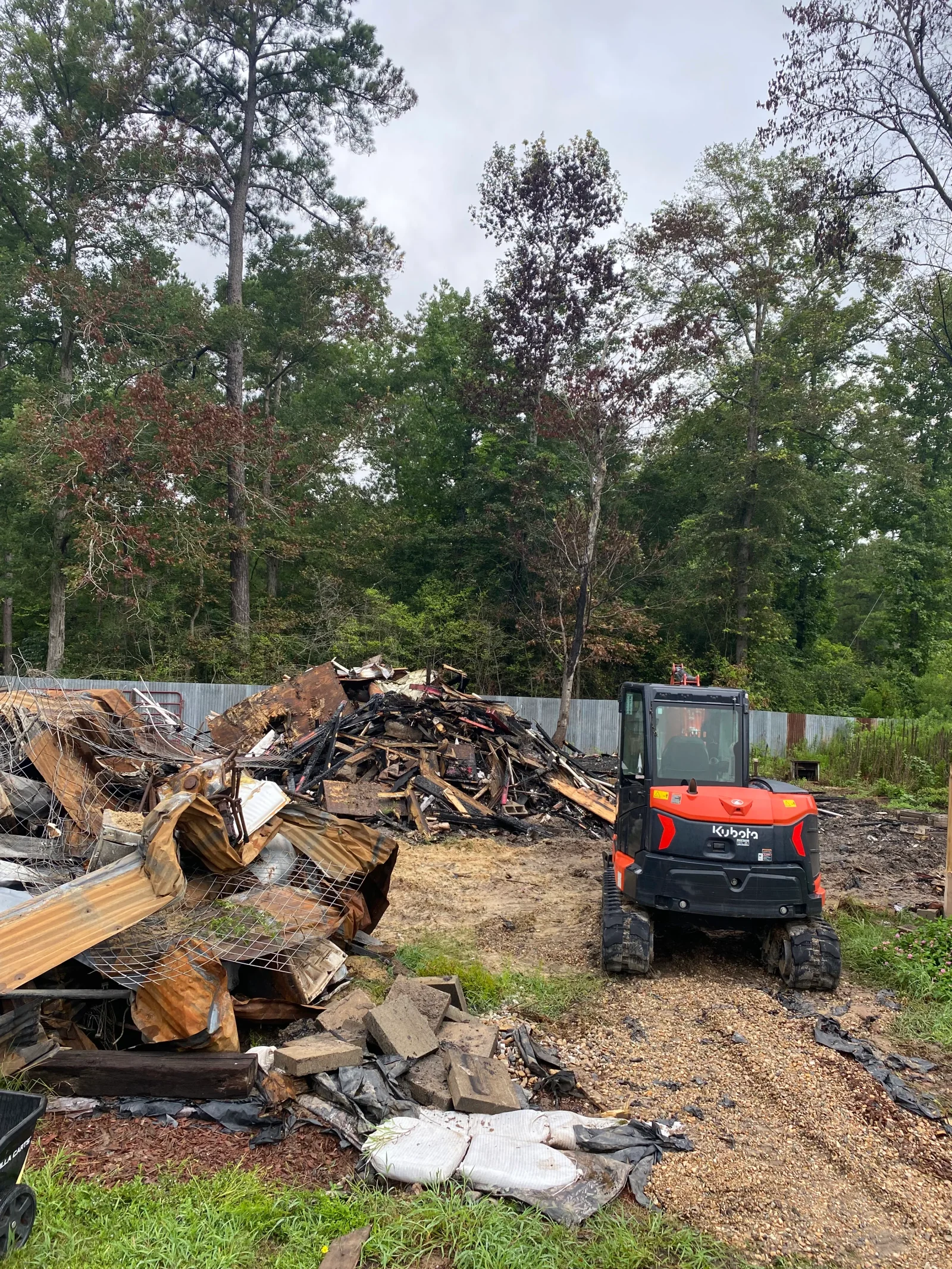 Demolition site with sorted debris piles, wood scraps, metal materials, and Kubota loader on gravel surface