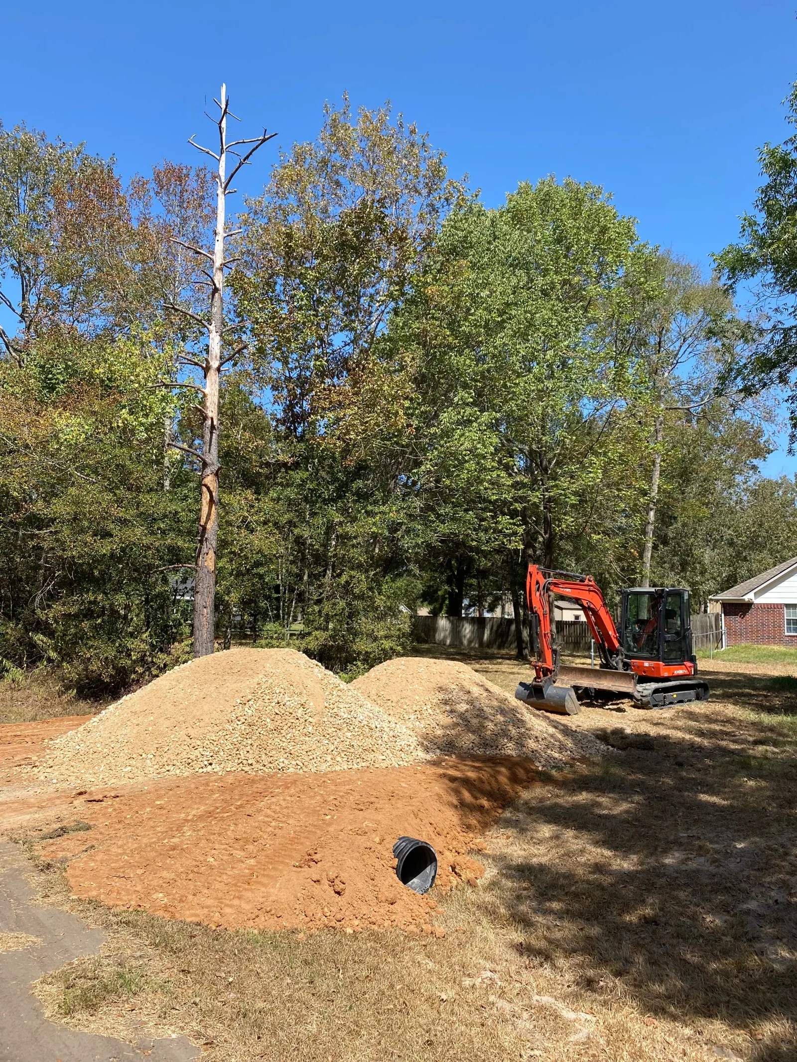 Dead tree removal with excavator, gravel stockpiles, and site grading on residential property