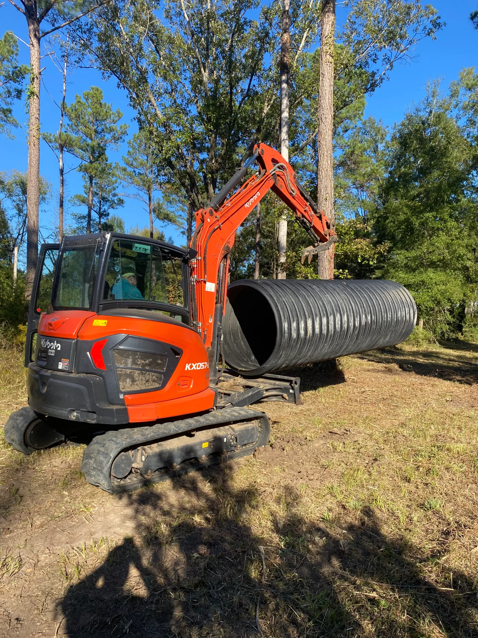 Kubota excavator placing corrugated metal drainage pipe in wooded area