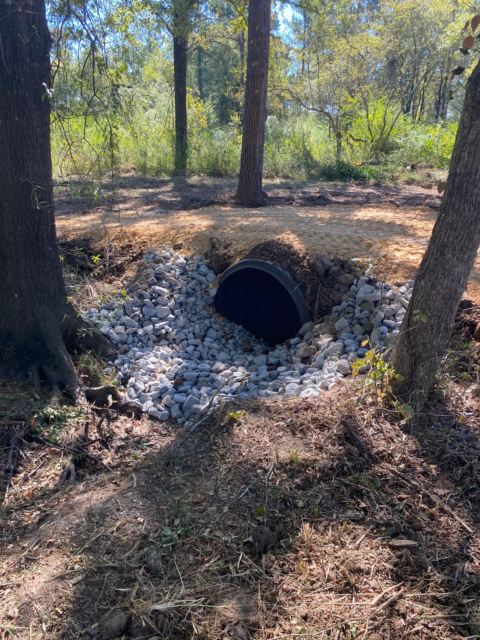 Black corrugated drainage pipe installed in wooded area with river rock and gravel base